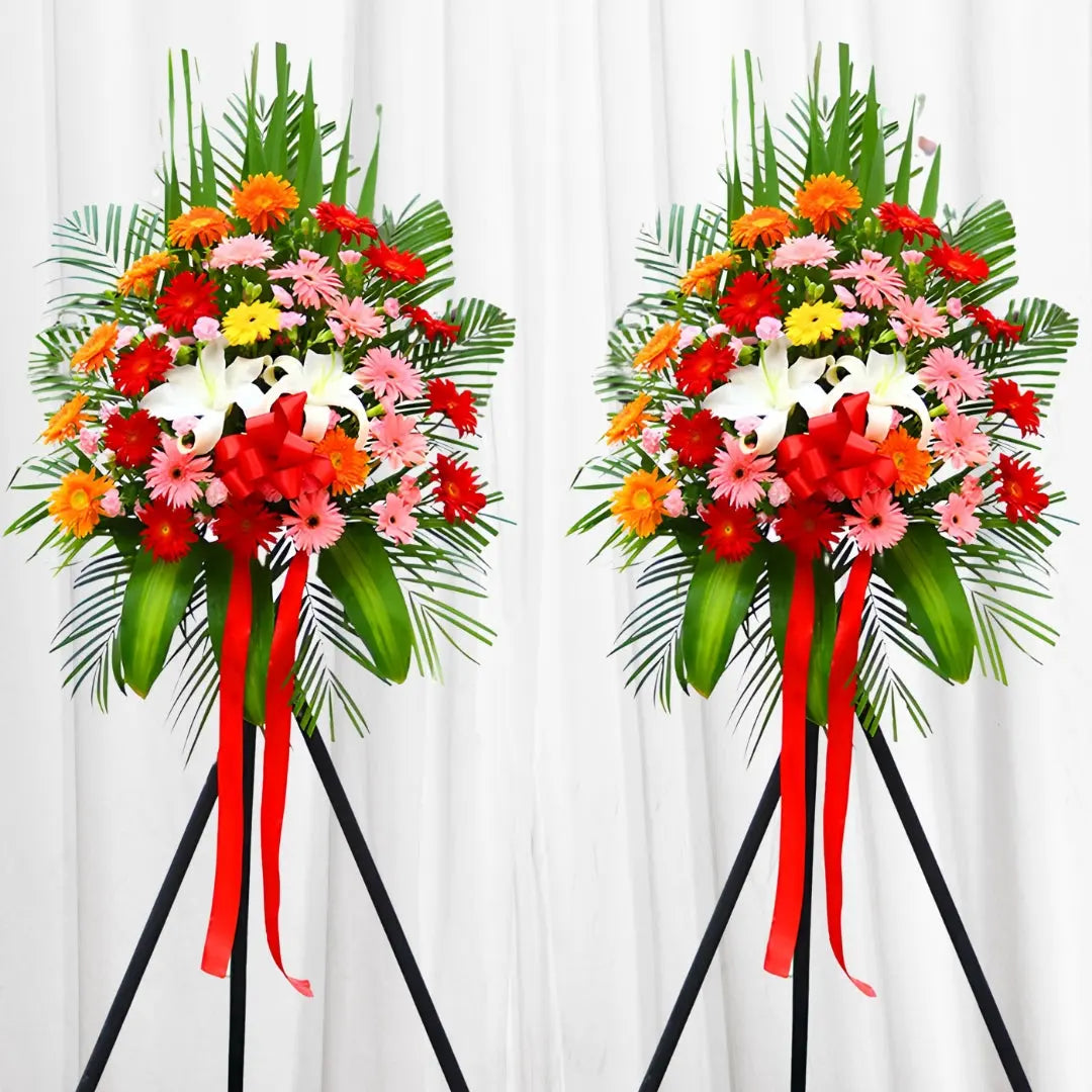 Vibrant Celebration Bouquet with red Gerbera daisies, white lilies, palm leaves, and red ribbons.